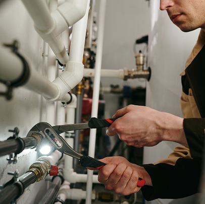 Person using pliers to tighten or loosen a pipe fitting on a wall with multiple pipes in an MEP and construction setting.
