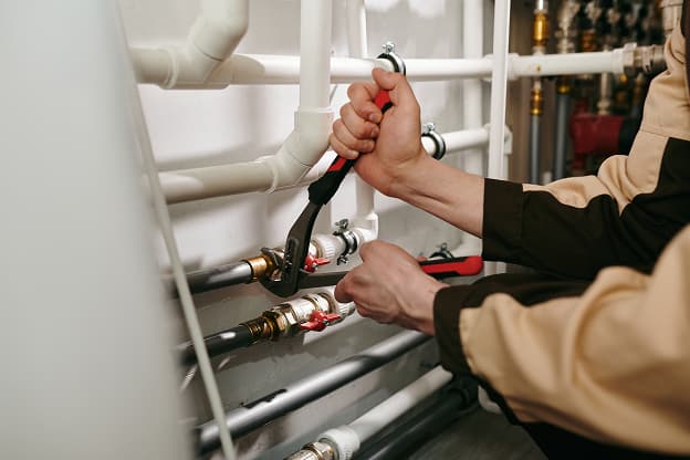 Person using pliers to adjust valves on a set of white and silver pipes in an indoor plumbing system, highlighting the hands-on aspect of MEP work.