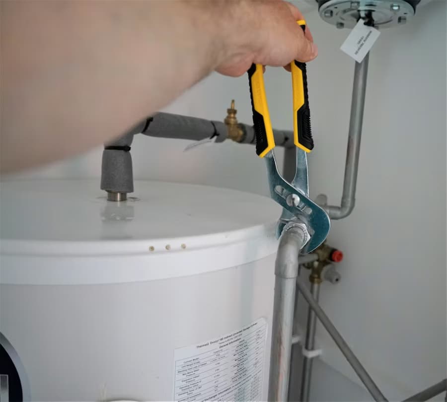 A person uses a pair of pliers to tighten a pipe connection on top of a white water heater as part of an MEP project in Colorado.