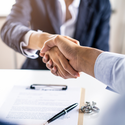 Two people in business attire shake hands over a contract on a desk, with a pen and a set of keys visible in the foreground, sealing a colorado electrical agreement.