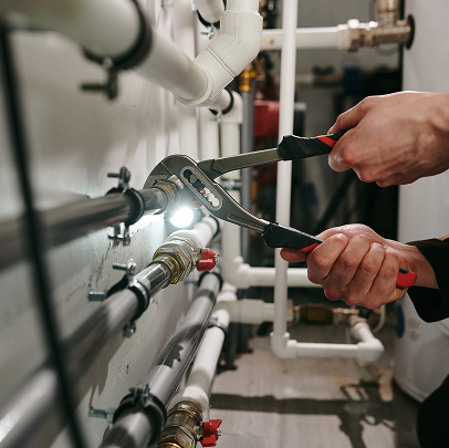 Person using pliers to tighten a metal pipe fitting on an MEP network of pipes in a utility or mechanical room in Colorado.