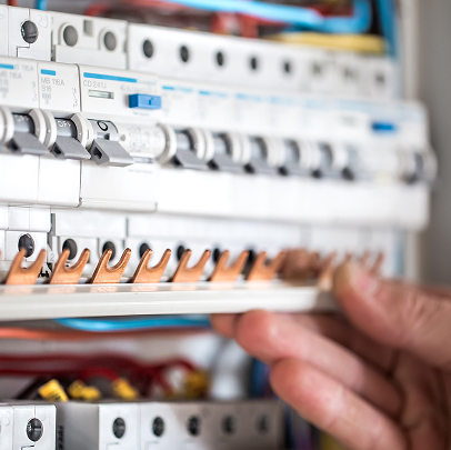 A hand adjusting a row of circuit breakers inside an electrical panel, with visible wiring and copper connectors, showcases the importance of electrical work in MEP systems.