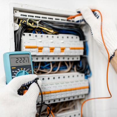 Person wearing gloves measures voltage in an electrical panel with a digital multimeter, which displays a reading of 222.7—a common scene in construction and MEP work.